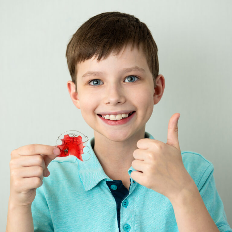 Boy Smiling Holding A Retainer Giving A Thumbs Up